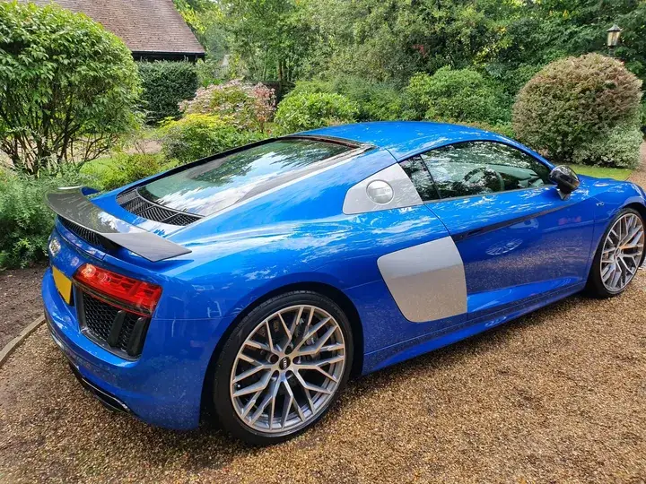 Rear three-quarter view of a gleaming blue Audi R8 with its rear wing