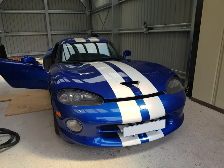 Blue Dodge Viper GTS with white racing stripes parked in a garage