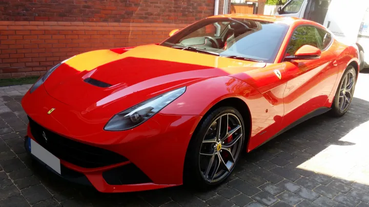 Red Ferrari F12berlinetta gleaming in the sun on a block-paved driveway