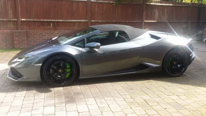 Side view of a grey Lamborghini Huracán Spyder with green brake calipers on a block-paved driveway