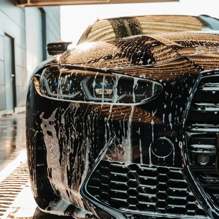 Black car covered in snow foam during a hand wash